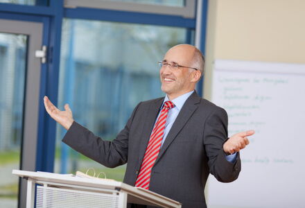 Mann mit ausgebreiteten Armen steht an einem Rednerpult beim Persönlichkeitstraining
